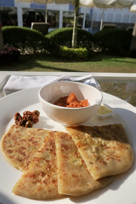 印度德里，北印度自助早餐，白色盘子里的aloo parathas切片与番茄酸辣酱，美味的面包塞满了garam masala土豆，酒店餐厅自制aloo paratha菜，raita凝乳酸奶，辣泡菜
